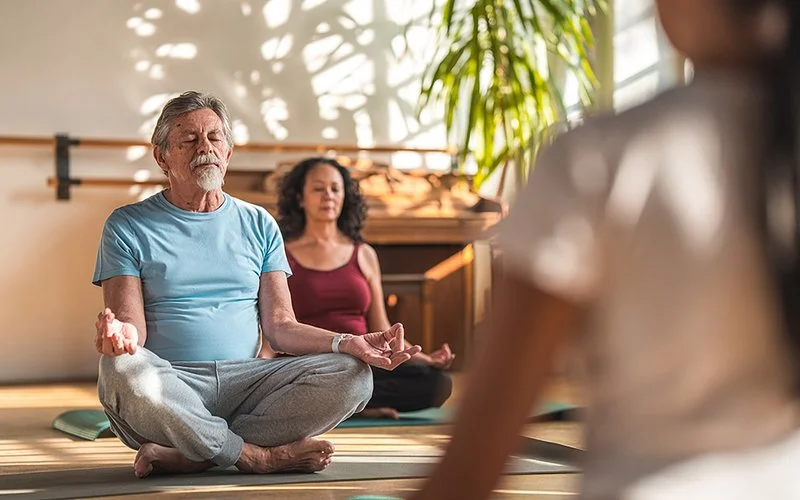 Ein Mann und eine Frau sitzen in einem Meditationsstudio auf Yogamatten im Lotussitz und meditieren mit geschlossenen Augen.