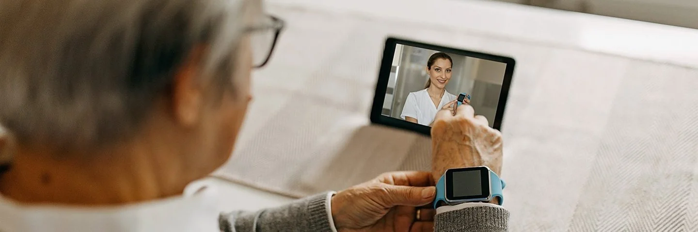 Blick über die Schulter einer älteren Person, die einen Videocall mit einer medizinischen Fachkraft auf einem Tablet durchführt.