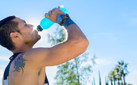 Ein sportlich gekleideter junger Mann trinkt ein blaues isotonisches Getränk aus einer Plastikflasche.