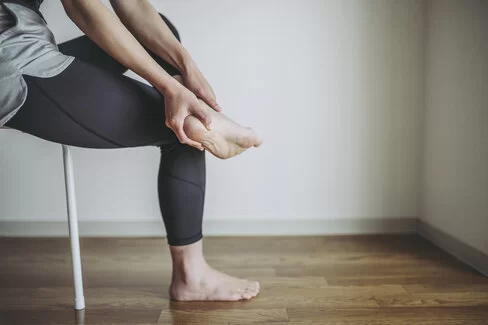 Eine Frau berührt ihre Ferse. Bei Schmerzen hilft die Stoßwellentherapie.