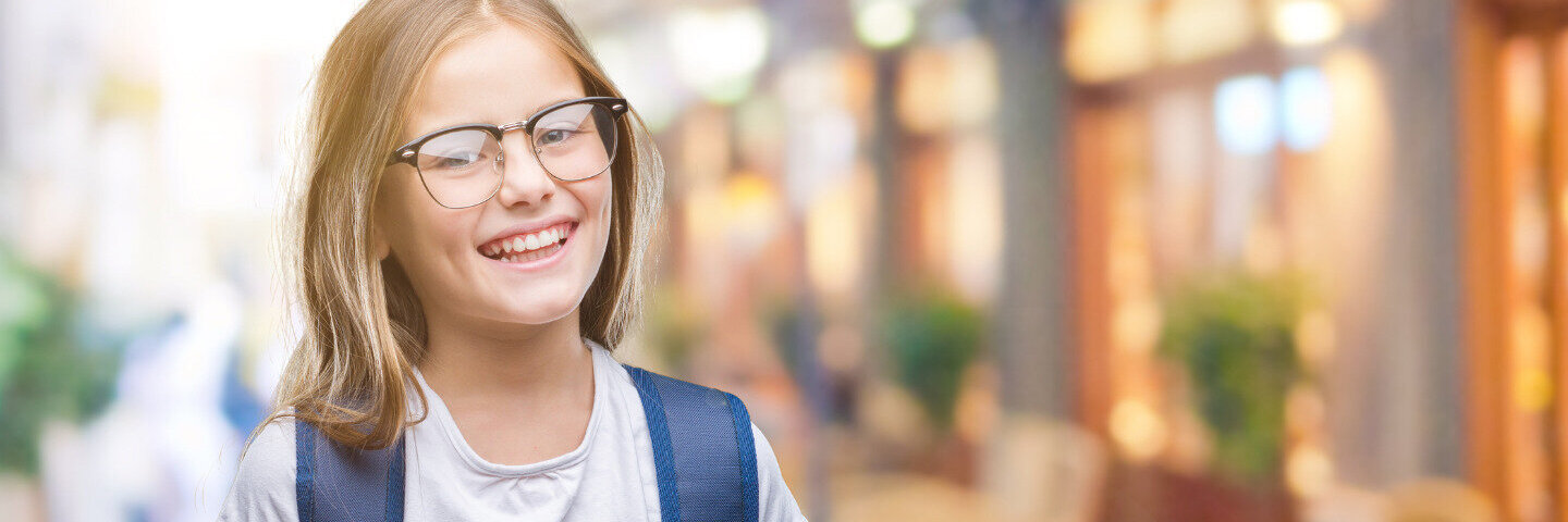 Ein Mädchen mit Sehschwäche und Brille grinst in die Kamera.