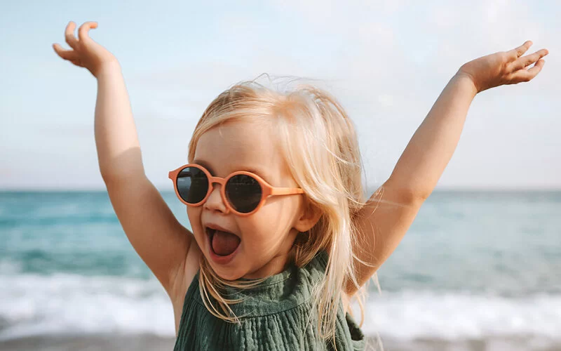 Ein kleines Mädchen mit Sonnenbrille am Strand.