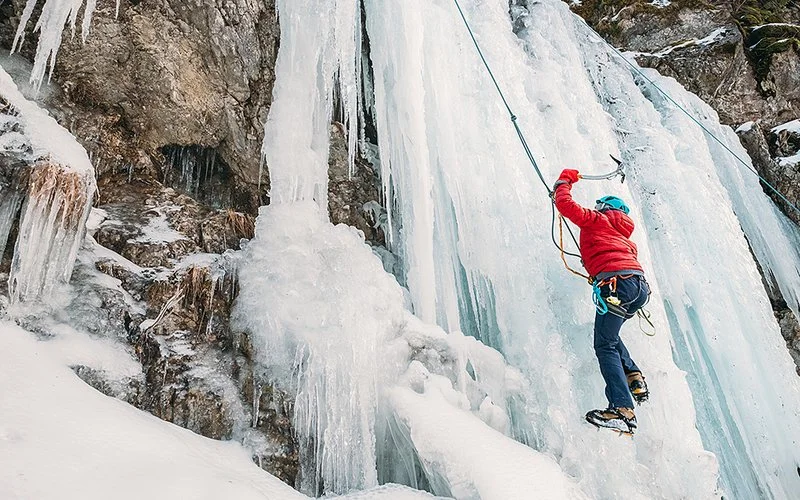 Ein Mann in Sicherheitsausrüstung steigt einen gefrorenen Wasserfall hinauf.
