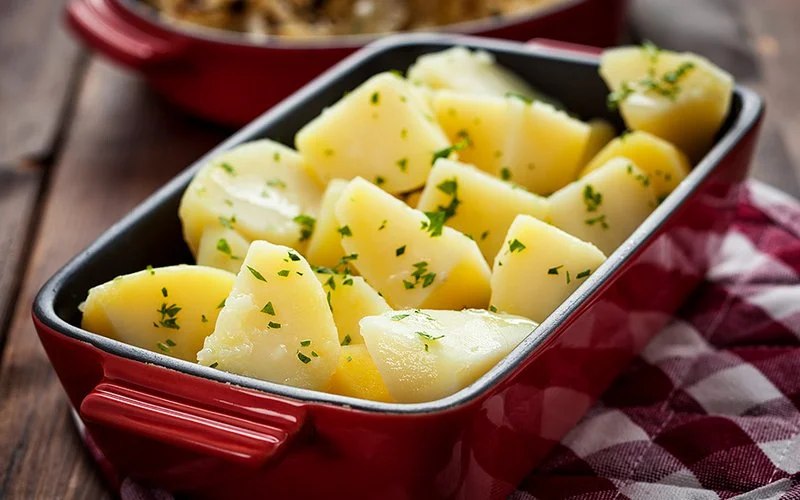 Geschälte und in Stücke geschnittene Salzkartoffeln mit gehackter Petersilie in einer rechteckigen Auflaufform.