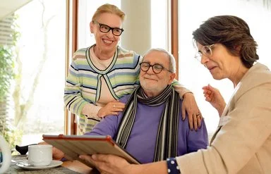 Eine Pflegeberaterin der AOK und ein lächelndes, älteres Ehepaar schauen auf ein Tablet.