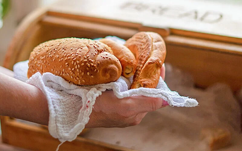 Frau bewahrt Brot und Brötchen im Brotkasten auf, weil sie weiß, dass beides länger frisch bleibt.