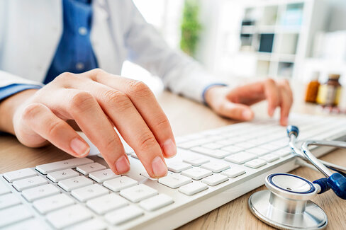 Eine Ärztin tippt auf eine Tastatur. Daneben liegt ein Stethoskop. Das Fachärzteteam von AOK-Clarimedis ist per E-Mail erreichbar.