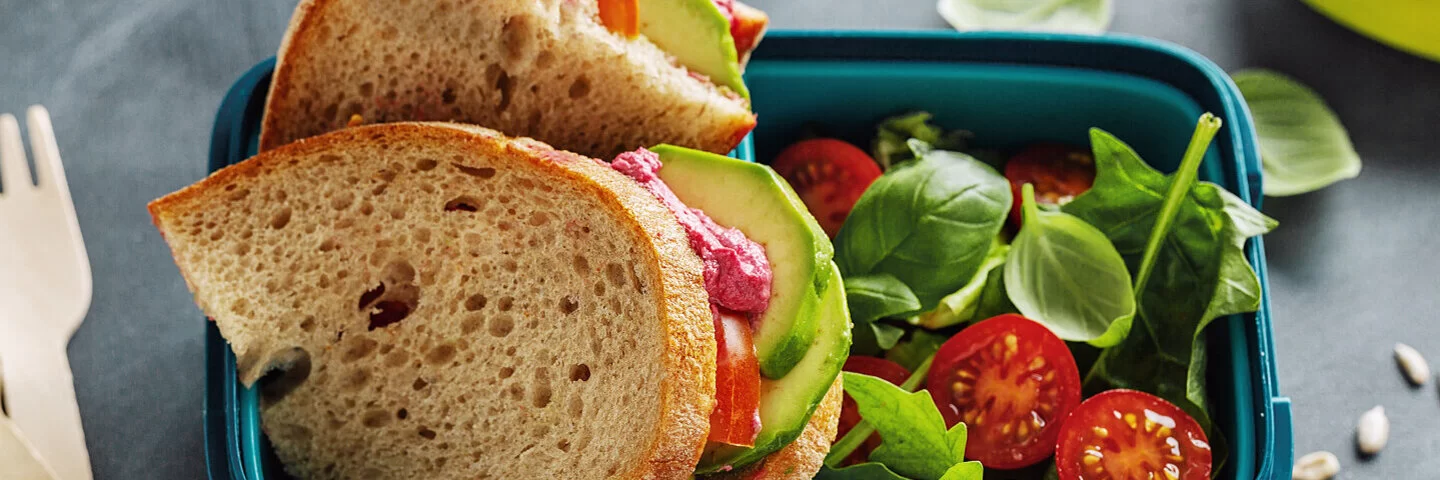 Zwei Scheiben Brot mit Avocado, Tomaten und Basilikum – ein gesundes Pausenbrot.