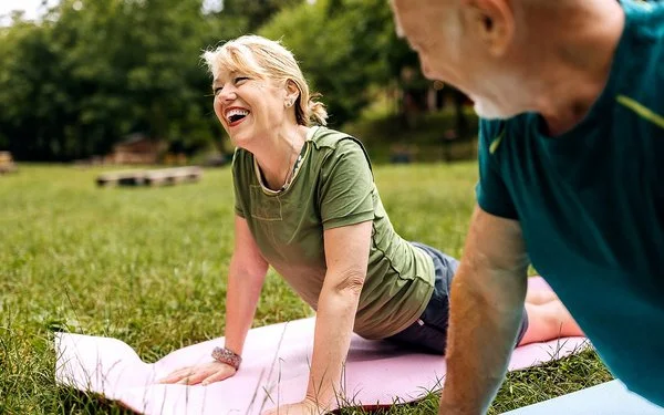 Ein sportlich gekleidetes Paar praktiziert Yoga im Park.