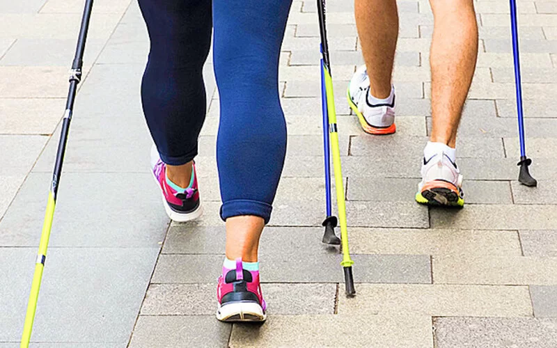 Beine von Personen beim Nordic Walking mit Trekkingstöcken.
