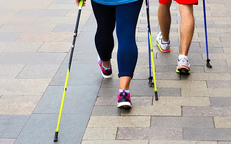Beine von Personen beim Nordic Walking mit Trekkingstöcken.