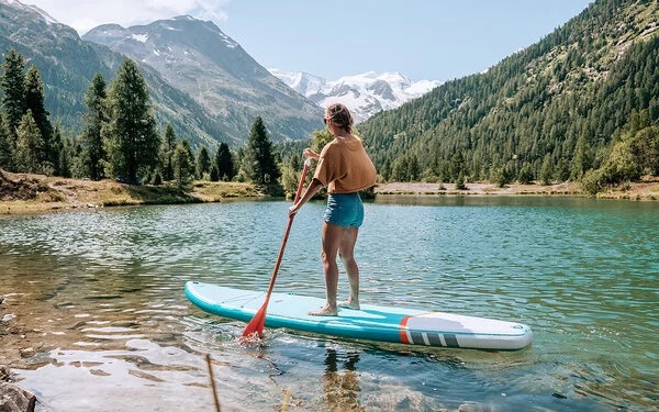 Eine junge Frau macht Stand-up-Paddling auf einem Bergsee.