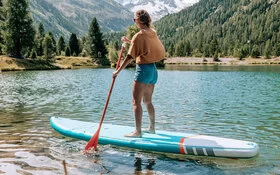 Eine junge Frau macht Stand-up-Paddling auf einem Bergsee.