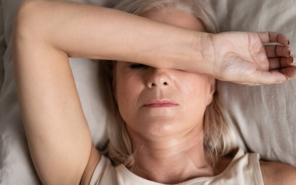 Frau in den Wechseljahren leidet unter Schlafstörungen und liegt im Bett mit dem Arm über dem Gesicht.