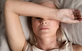 Frau in den Wechseljahren leidet unter Schlafstörungen und liegt im Bett mit dem Arm über dem Gesicht.