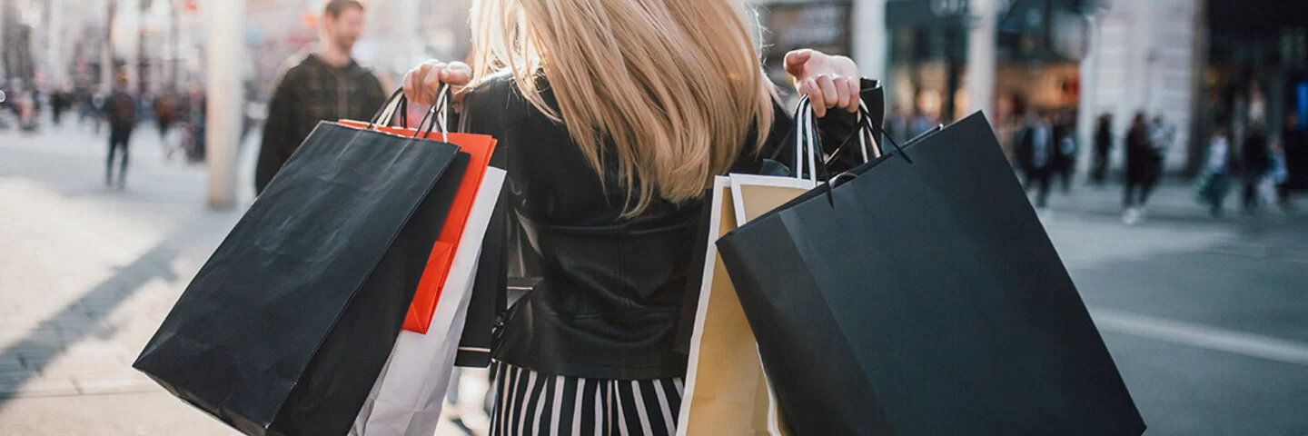 Eine Frau trägt mehrere Einkaufstaschen über den Schultern und schlendert durch eine Einkaufsstraße zum Shoppen