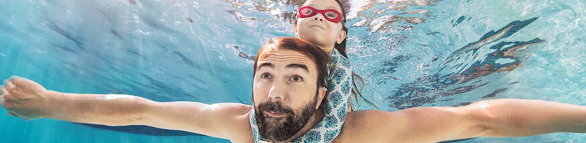 Ein Mann schwimmt unter Wasser. Ein Kind hält sich an seinen Schultern fest.