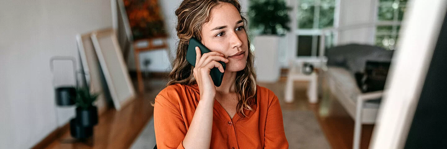 Eine junge Frau sitzt mit Smartphone am Schreibtisch. Beim Clarimedis-Info-Telefon erhält sie fachärztliche Auskünfte.