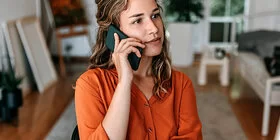 Eine junge Frau sitzt mit Smartphone am Schreibtisch. Beim Clarimedis-Info-Telefon erhält sie fachärztliche Auskünfte.