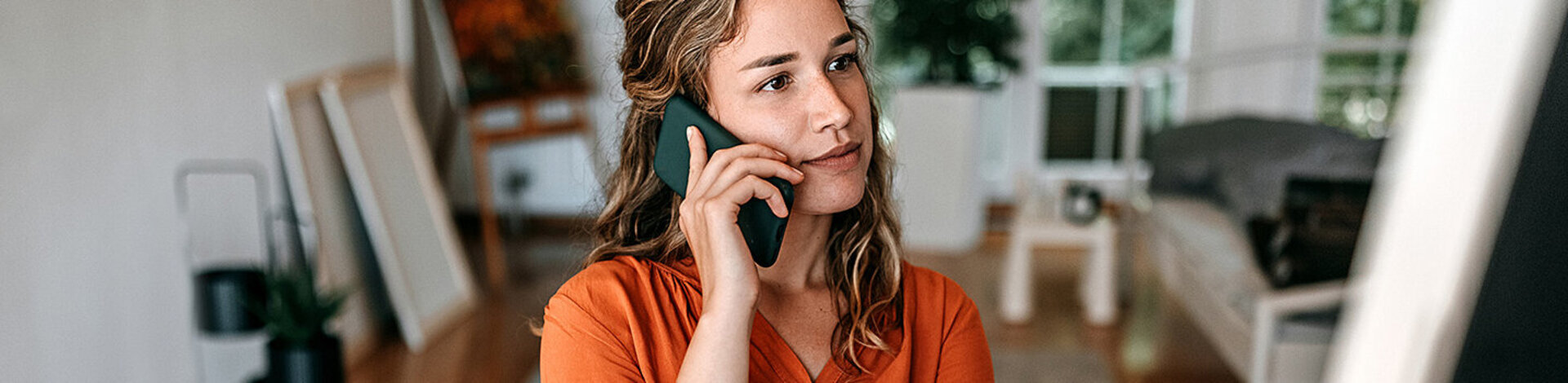 Eine junge Frau sitzt mit Smartphone am Schreibtisch. Beim Clarimedis-Info-Telefon erhält sie fachärztliche Auskünfte.