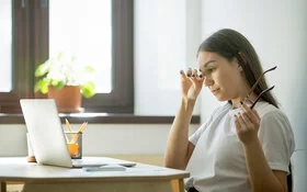 Eine Frau hat die Brille abgenommen und reibt sich die Augen.