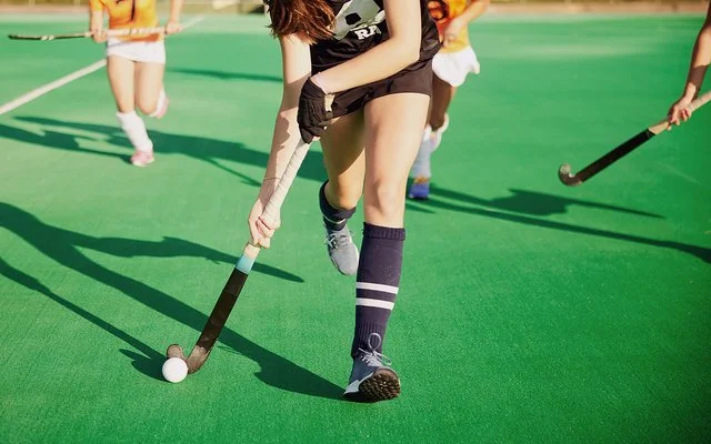 Zwei Damenmannschaften laufen mit Feldhockeyschlägern einem Ball hinterher.