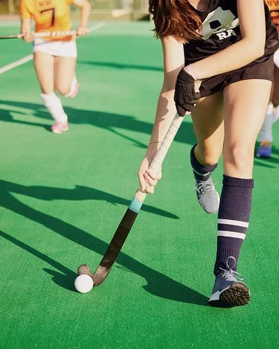 Zwei Damenmannschaften laufen mit Feldhockeyschlägern einem Ball hinterher.