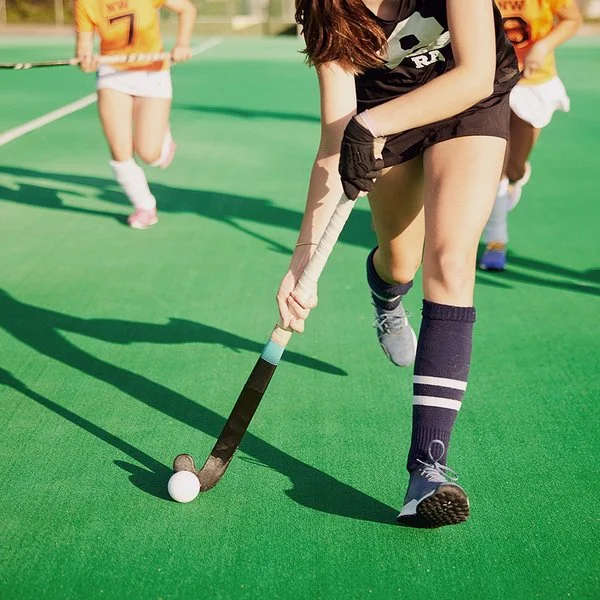 Zwei Damenmannschaften laufen mit Feldhockeyschlägern einem Ball hinterher.