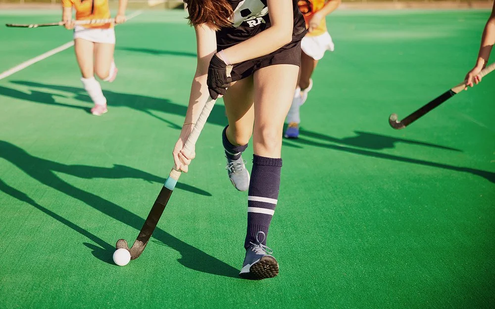 Zwei Damenmannschaften laufen mit Feldhockeyschlägern einem Ball hinterher.