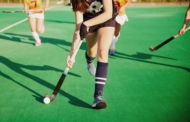 Zwei Damenmannschaften laufen mit Feldhockeyschlägern einem Ball hinterher.