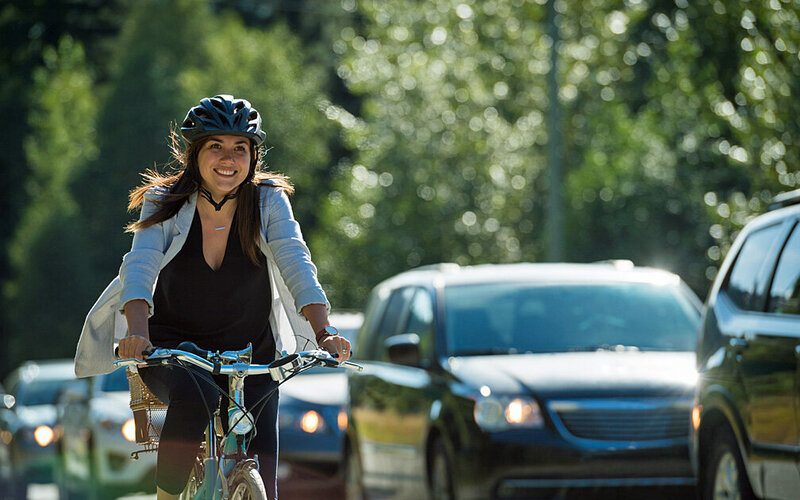 Eine Frau mit Helm fährt Fahrrad statt Auto und trägt so zum Umweltschutz bei.