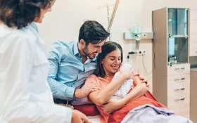 Eine junge Familie auf der Geburtsstation im Krankenhaus. Die Frau hält ihr neugeborenes Baby im Arm.