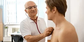 Ein Mann untersucht einen Patienten mit dem Stethoskop. Mit der Hausarztzentrierten Versorgung (HzV) unterstützt die AOK insbesondere chronisch kranke Patienten.