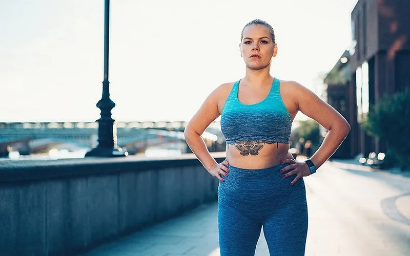 Eine Frau steht selbstbewusst mit den Armen in der Taille auf der Straße.