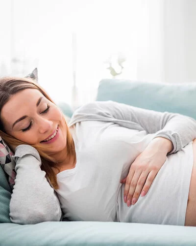 Schwangere Frau liegt lächelnd auf der Couch und streichelt ihren Bauch.