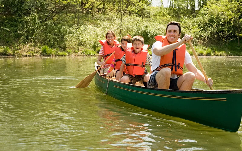 Vierköpfige Familie mit Schwimmwesten paddelt mit einem Kanu auf einem Fluß.