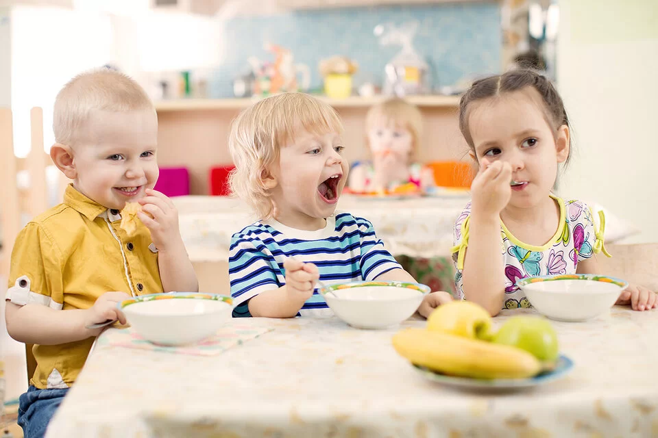 Drei Kinder im Kitaalter sitzen am Tisch und essen Obst.