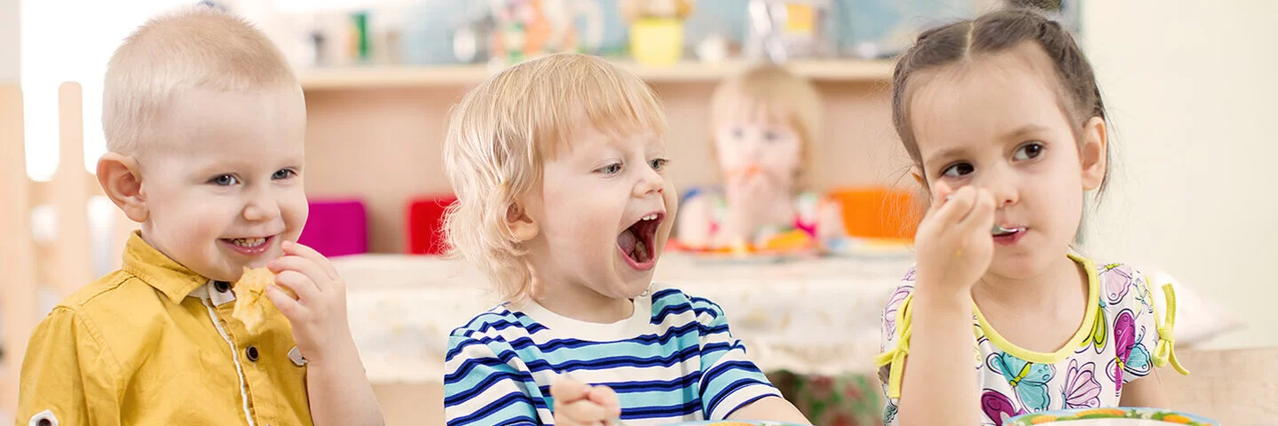 Drei Kinder im Kitaalter sitzen am Tisch und essen Obst.