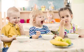 Drei Kinder im Kitaalter sitzen am Tisch und essen Obst.
