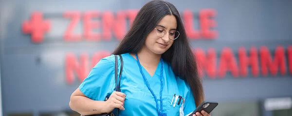 Die Pflegefachfrau Assia Arslan verlässt am Morgen nach der Nachtschicht im Pflegekittel das Krankenhaus. Sie schaut auf ihr Smartphone.