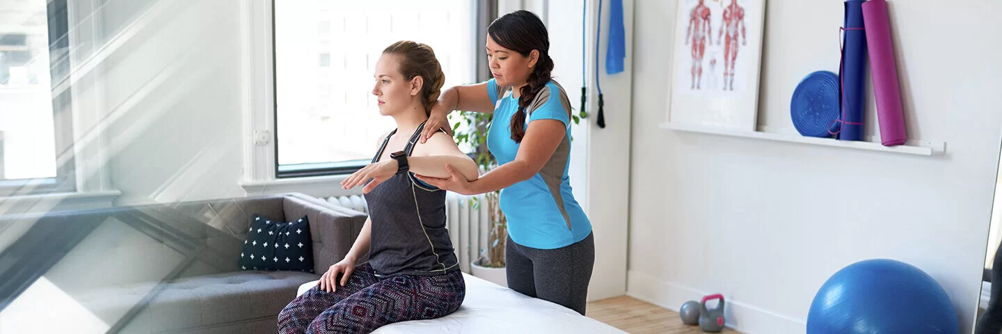 Chinesische Frau Physiotherapie Professionelle gibt eine Behandlung zu einem attraktiven blonden Kunden in einem hellen medizinischen Büro – Stockfoto