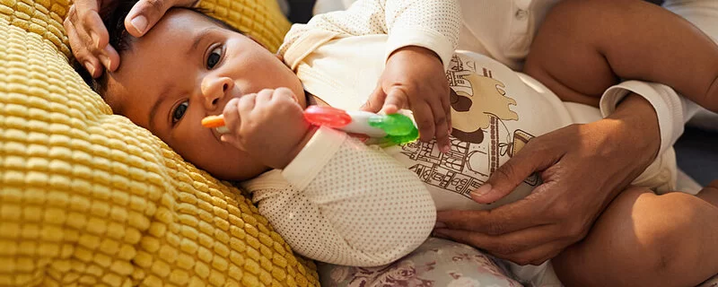 Zahnendes Baby im Arm der Mutter kaut auf einem Beißring herum.