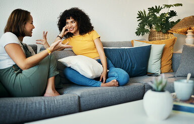 Ein Gespräch über Begriffe wie Schamlippen: Zwei junge Frauen sitzen auf dem Sofa und unterhalten sich.
