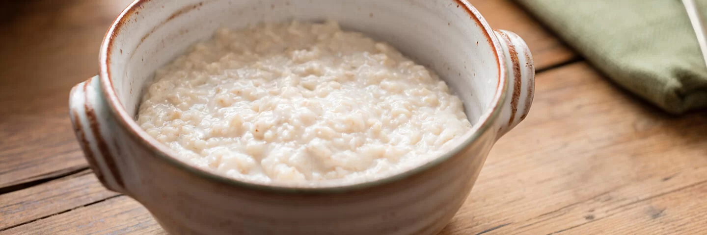 Eine kleine Porzellanschale gefüllt mit Haferbrei auf einem Holzuntergrund.