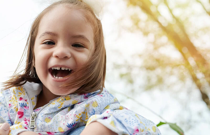 Ein fröhlich lächelndes, etwa drei Jahre altes Mädchen mit einer Zahnlücke zwischen den Schneidezähnen.