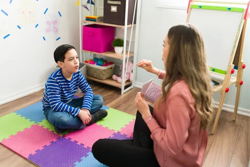 Ein Junge sitzt einer Frau gegenüber, sie sehen sich an und sprechen.