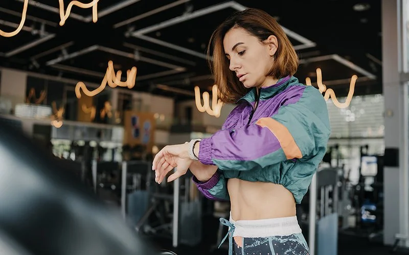 Eine sportliche Frau checkt im Fitnessstudio ihre Smart Watch.