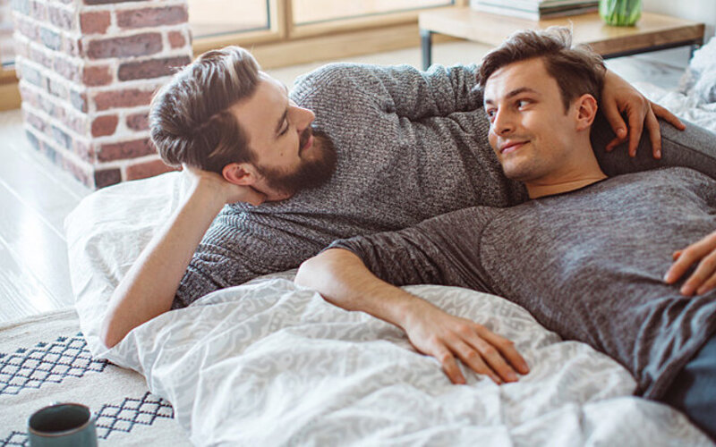Ein schwules Paar kuschelt auf dem Bett.