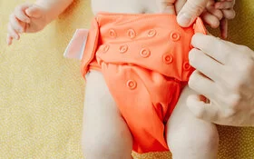 Baby wird mit einem orangefarbenem Windelhöschen gewickelt.