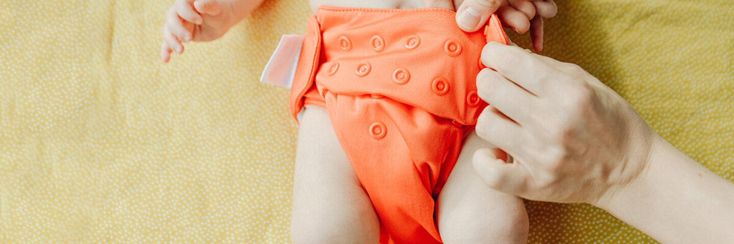 Baby wird mit einem orangefarbenem Windelhöschen gewickelt.